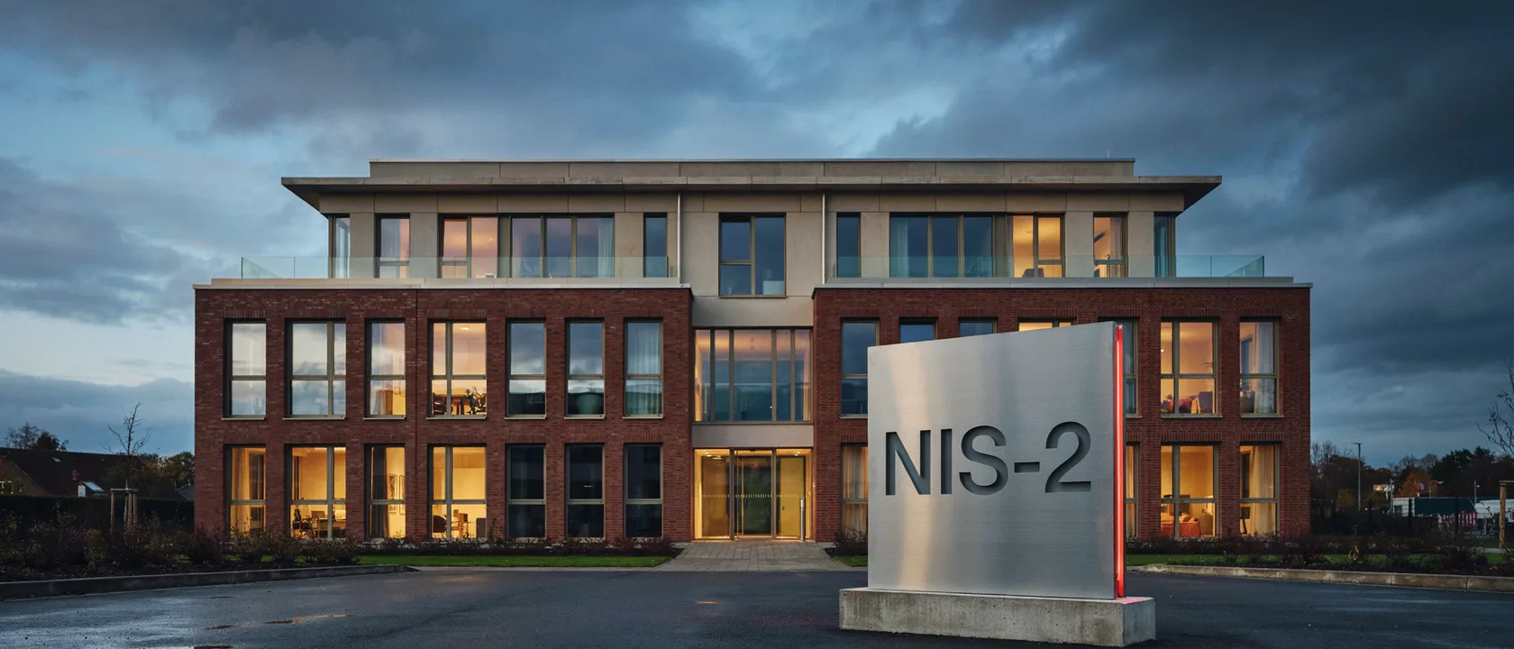 Bürogebäude eines Unternehmens in der Abenddämmerung mit Stele „NIS-2“ vor dem Eingang