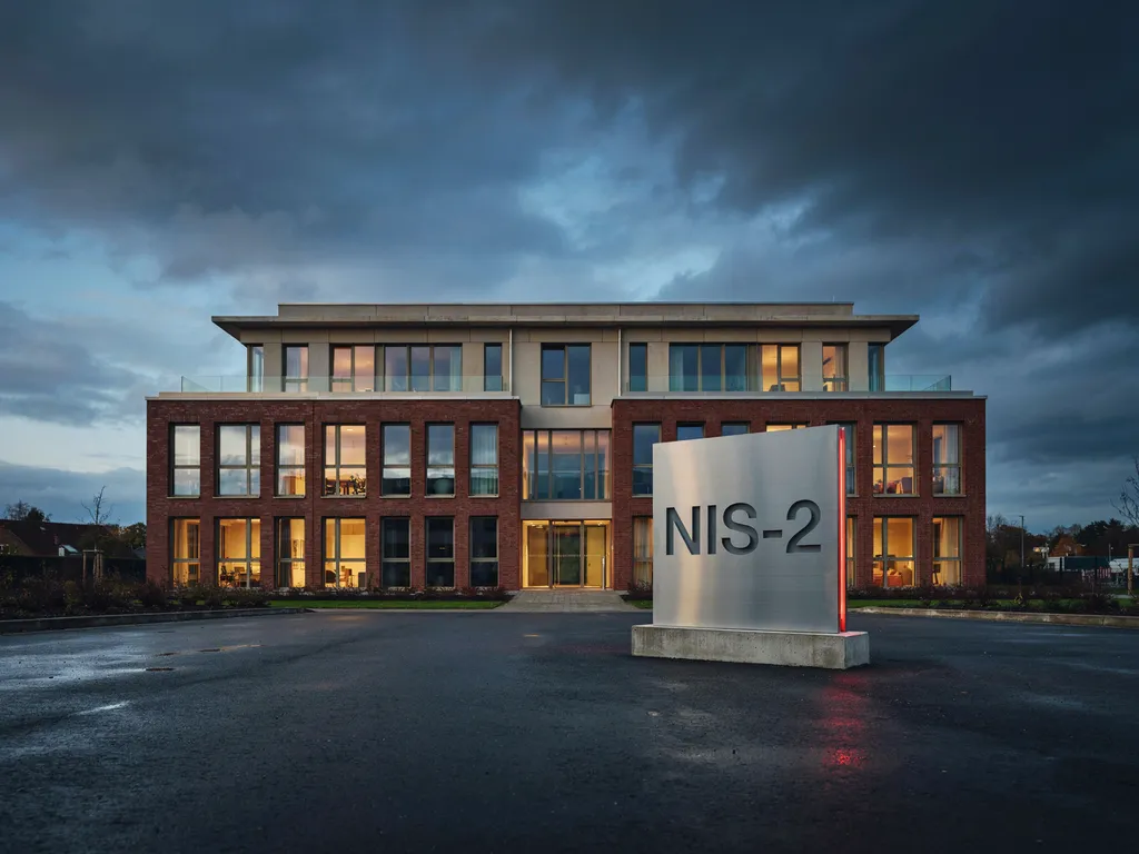 Bürogebäude eines Unternehmens in der Abenddämmerung mit Stele „NIS-2“ vor dem Eingang
